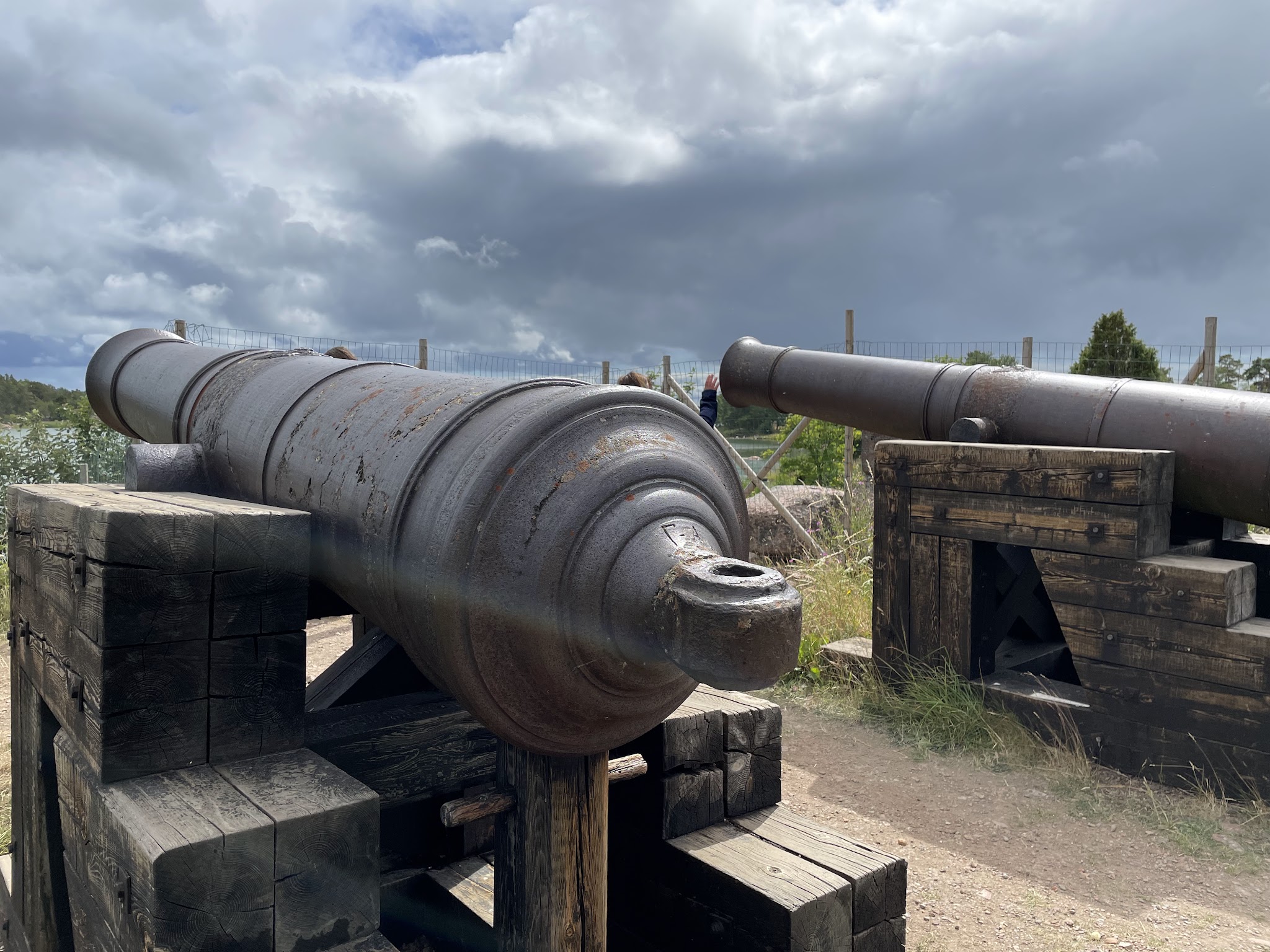 Zwei rostige historische Kanonen auf hölzernen Lafetten richten sich von einer Festungsanlage in die bewölkte Landschaft.