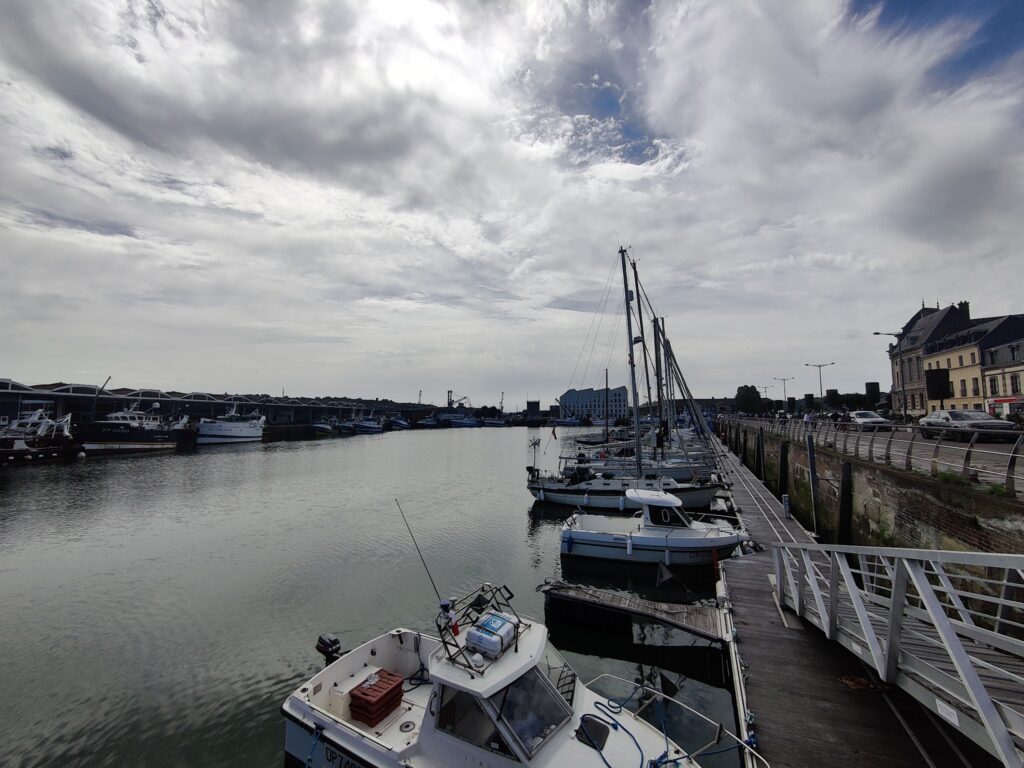 Segelboote liegen im Hafen an Holzsteg, bewölkter Himmel, Häuserzeile rechts entlang des Kais.