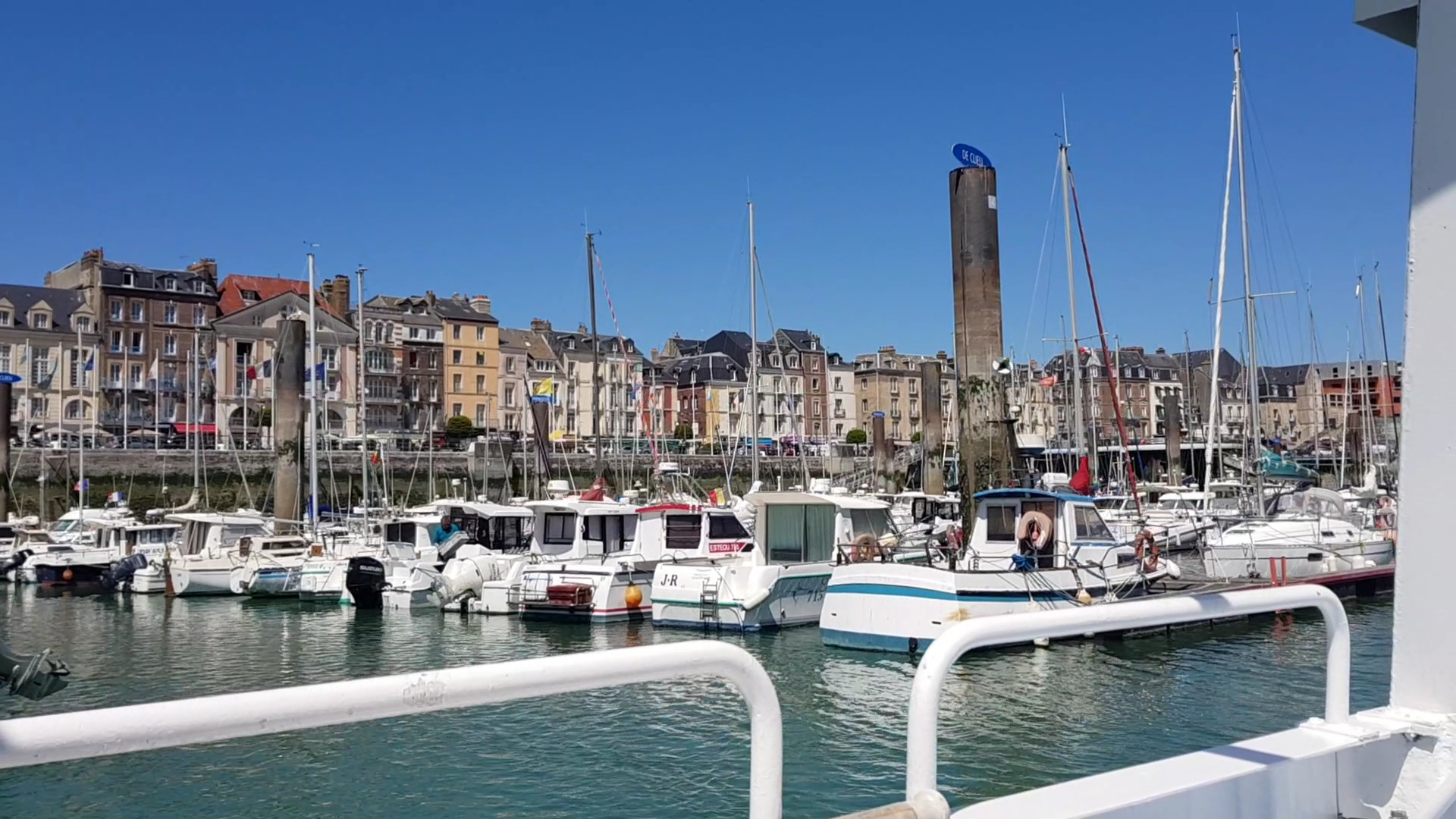 Kleine Motor- und Segelboote liegen im sonnigen Stadthafen vor einer Reihe bunter Altbauten.