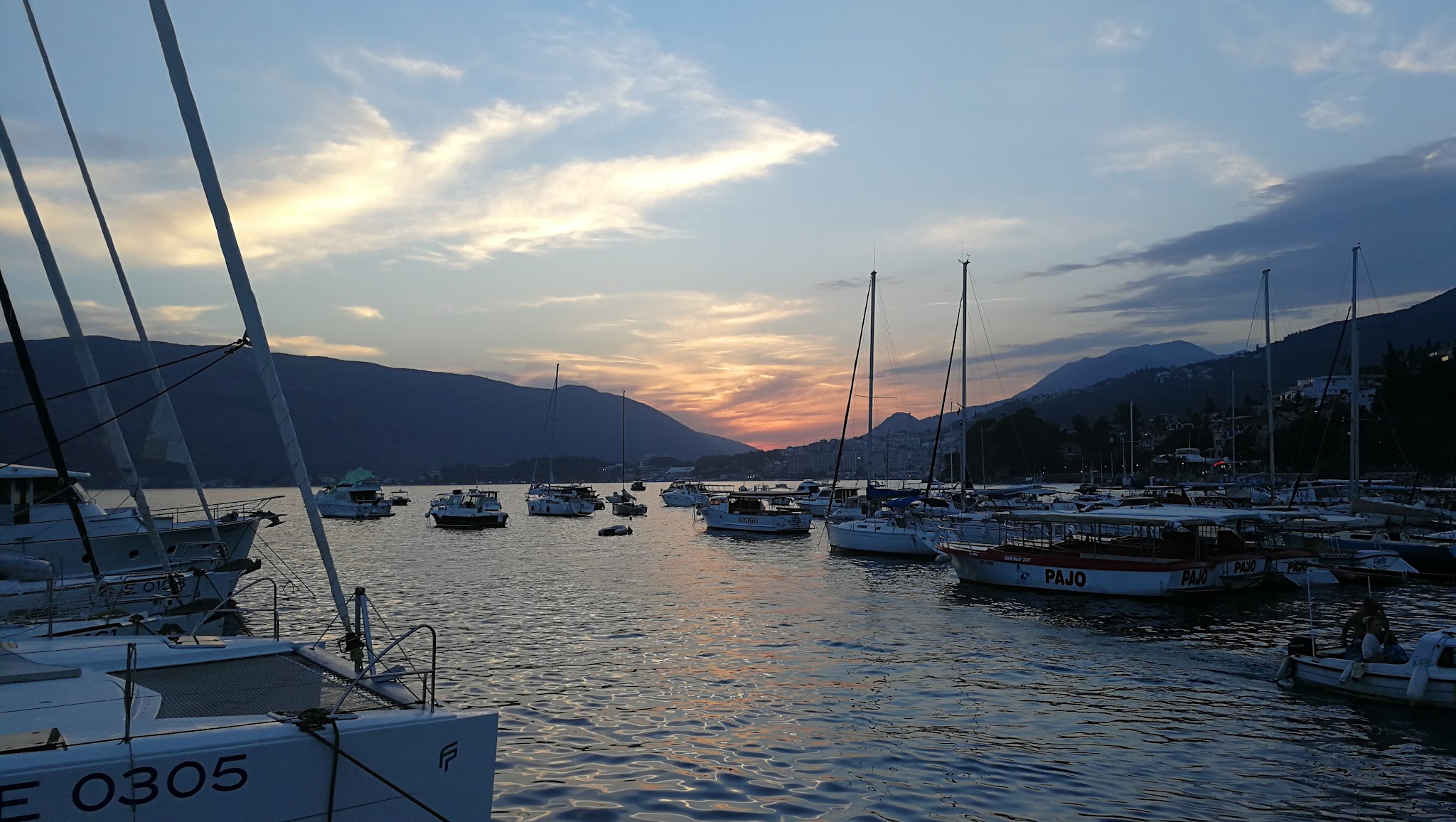 Hafen bei Sonnenuntergang; Segel- und Motorboote dümpeln, Berge im Hintergrund, Himmel rosa-blau