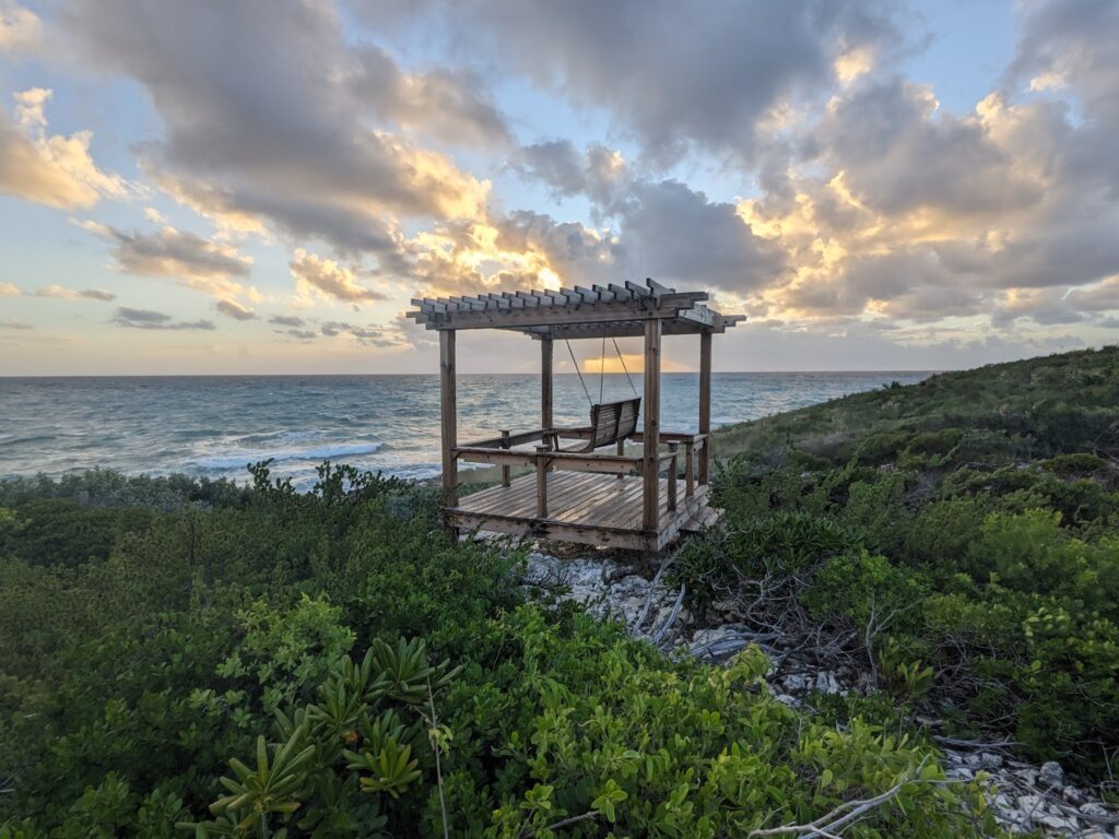 Holz-Pergola mit Hängeschaukel über grüner Küste, Blick auf wellige See unter dramatischer Abendwolke