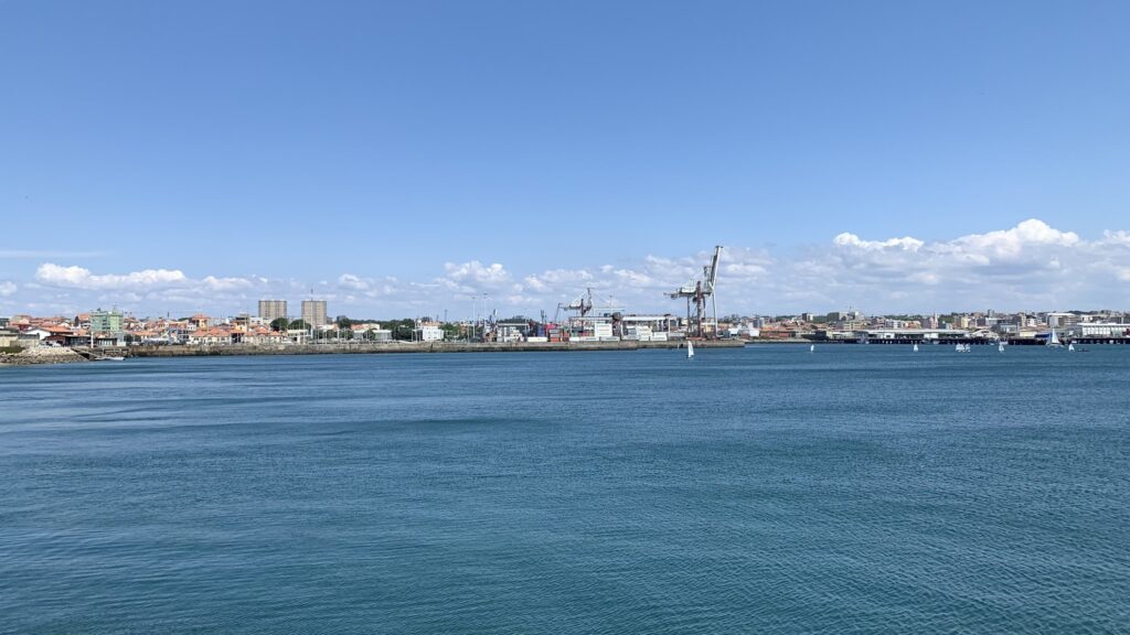 Hafenstadt mit Kränen, Containerterminals und kleinen Segelbooten auf ruhigem, türkisblauem Wasser unter klarem Himmel