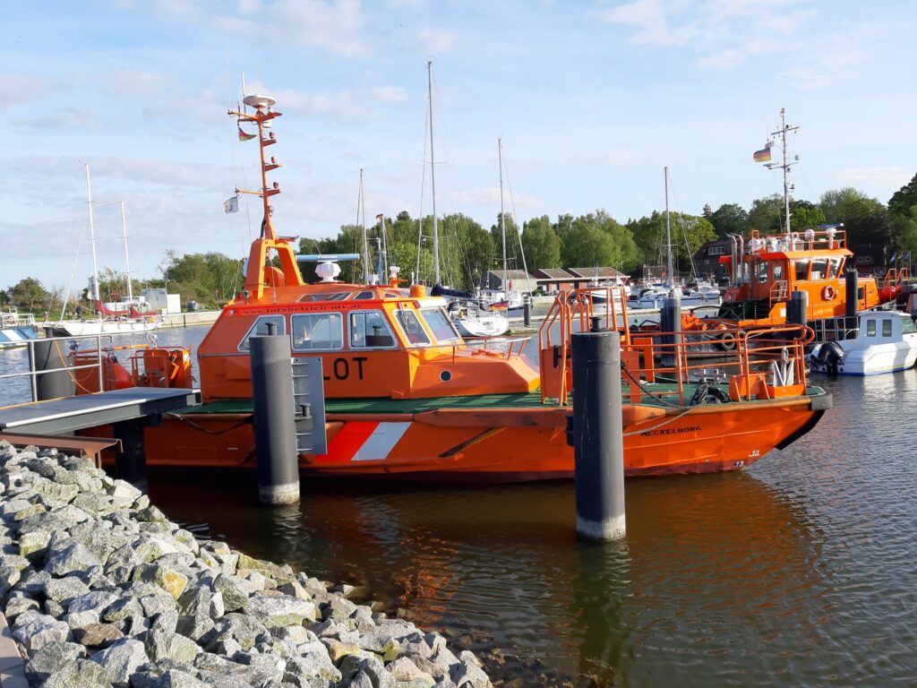 Orange Lotsenboot am Kai im sonnigen Yachthafen, umgeben von Segelbooten und ruhigem Wasser.