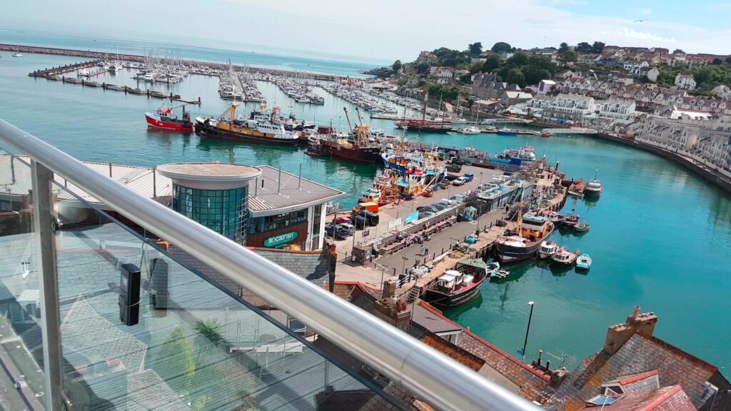 Überblick auf lebhaften Küstenhafen mit Fischerbooten, Yachten und terrassenförmigen Häusern am türkisfarbenen Wasser.
