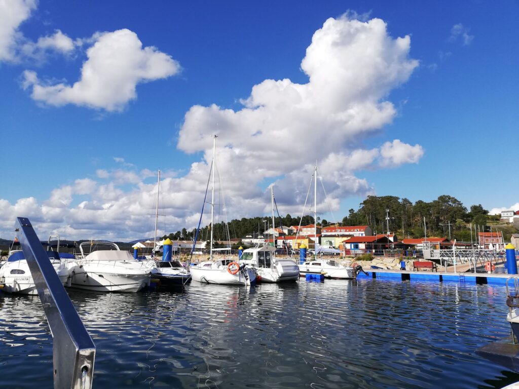 Mehrere Segel- und Motorboote liegen an blauem Pier im sonnigen Hafen, Wolken am klaren Himmel.