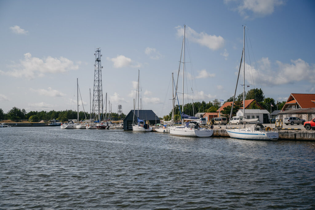 Kleiner Hafen mit mehreren vertäuten Segelbooten, Funkmast und Uferhäusern unter blauem Himmel.