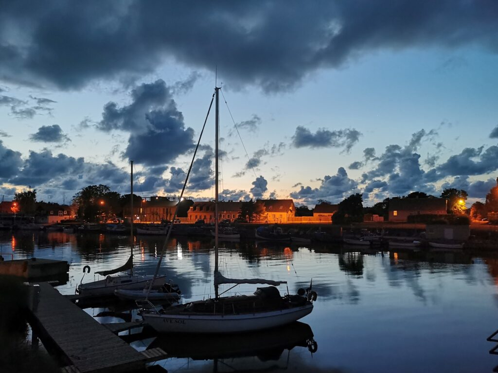 Abenddämmerung im Hafen, dunkle Wolken, beleuchtete Häuser, vertäute Segelboote spiegeln sich im ruhigen Wasser