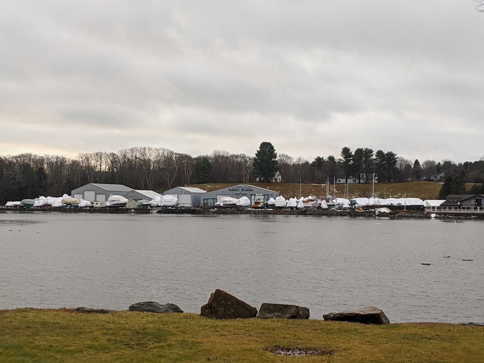 Marina am trüben Wintertag; zahlreiche weiß eingepackte Boote liegen gegenüber am Ufer.