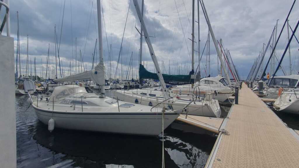 Segelboote liegen dicht an dicht in einer Marina; Steg rechts, bewölkter Himmel darüber.