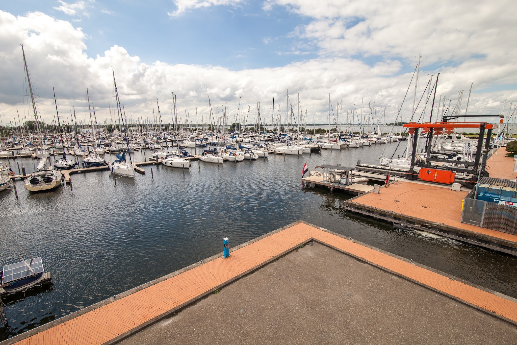 Große Marina: zahlreiche Segelboote an Stegen, ruhiges Wasser unter teils wolkigem Himmel.