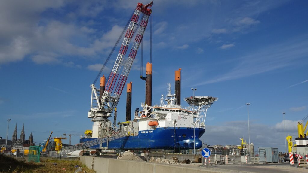 Offshore-Installationsschiff mit großem Kran und ausgefahrenen Stützbeinen im Hafen unter blauem Himmel