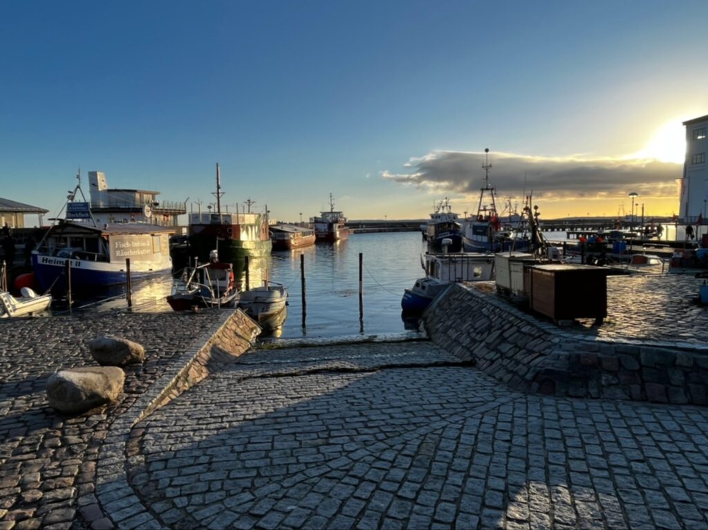 Kleiner Hafen in Abendsonne, mehrere Fischerboote an Stegen, Kopfsteinpflasterrampe im Vordergrund