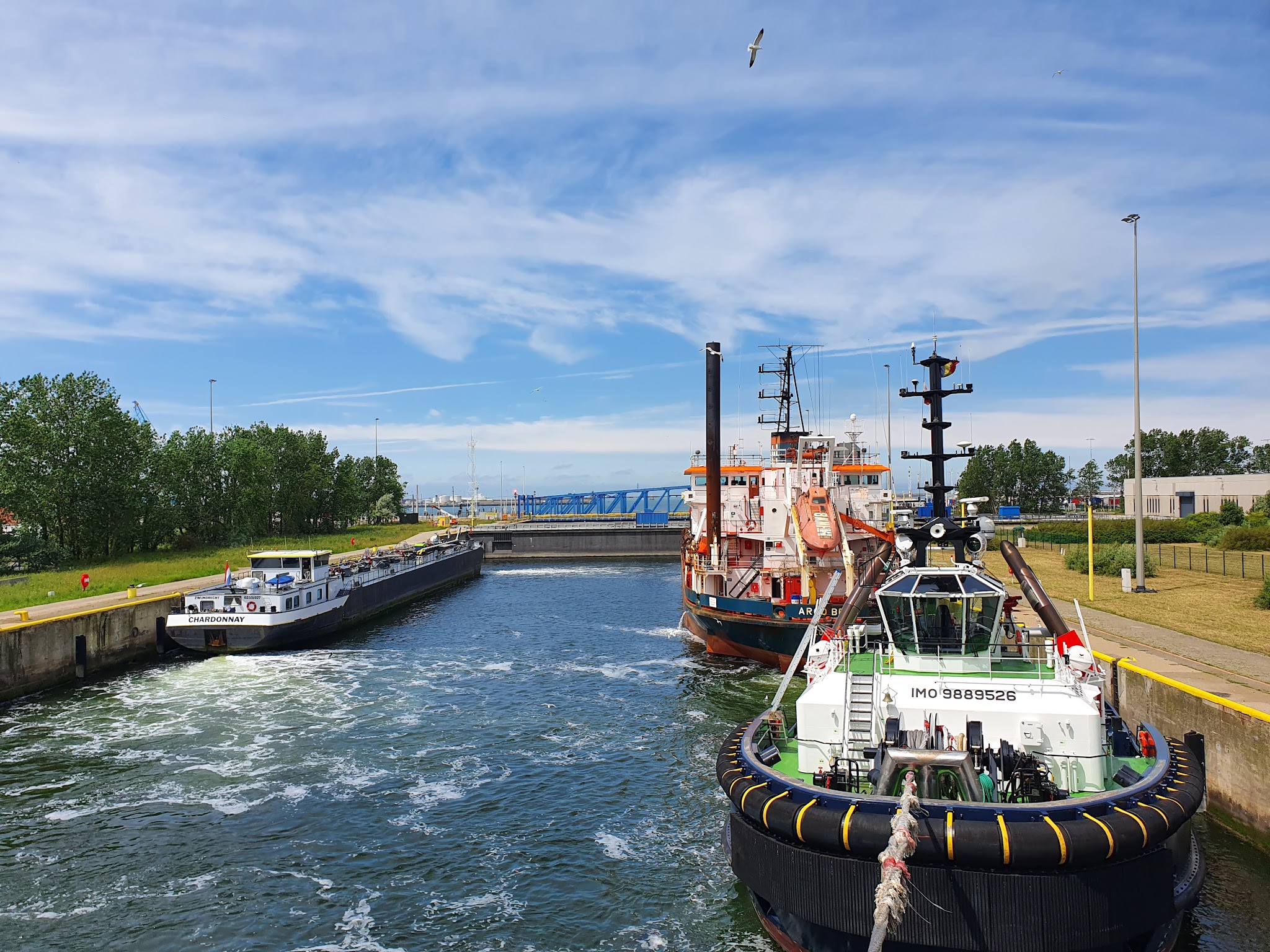 Drei Schiffe manövrieren dicht in einer Schleuse; vorn ein Schlepper, dahinter Versorgungsschiff und Frachter.
