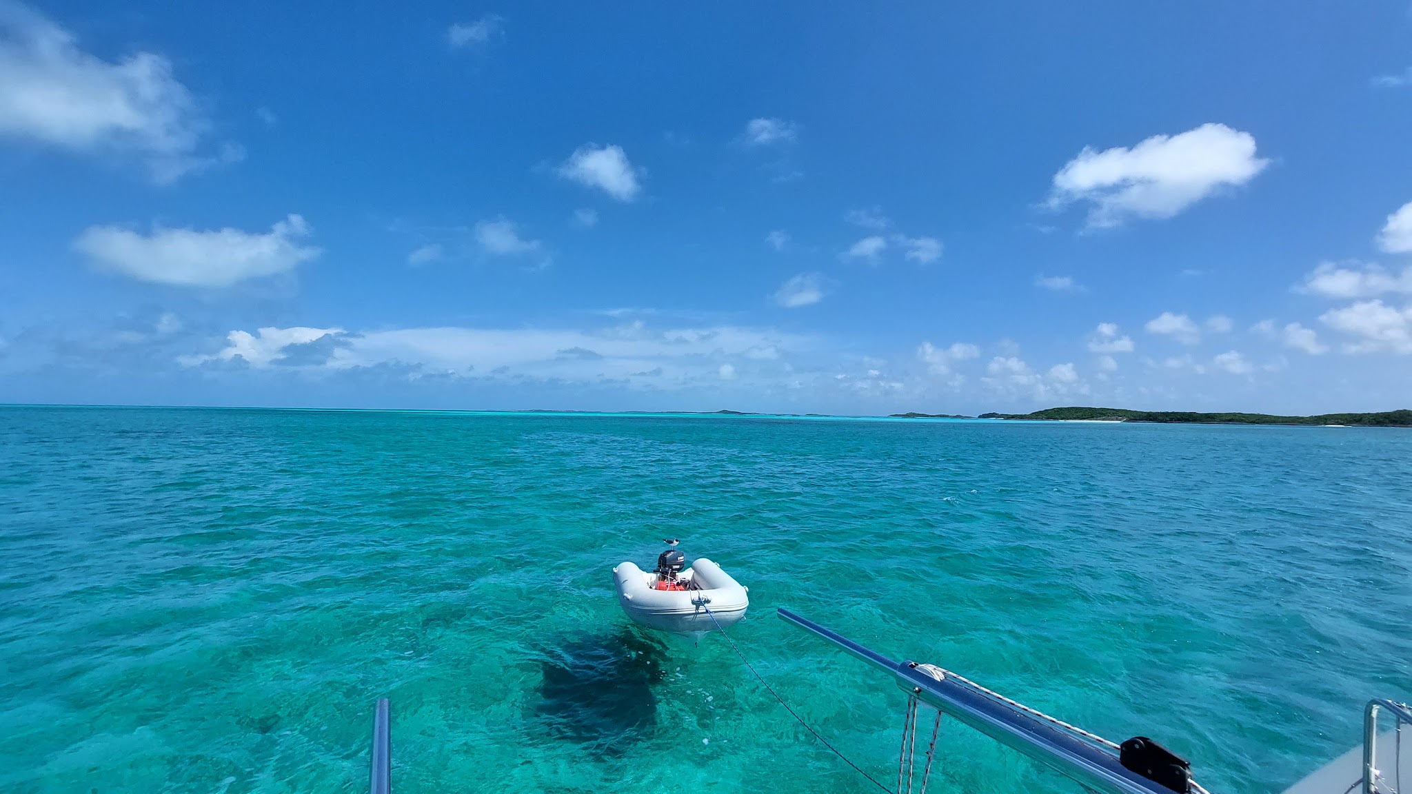 Klares türkisfarbenes Meer; ein angebundenes Schlauchboot treibt, ferne flache Inseln unter blauem Himmel.