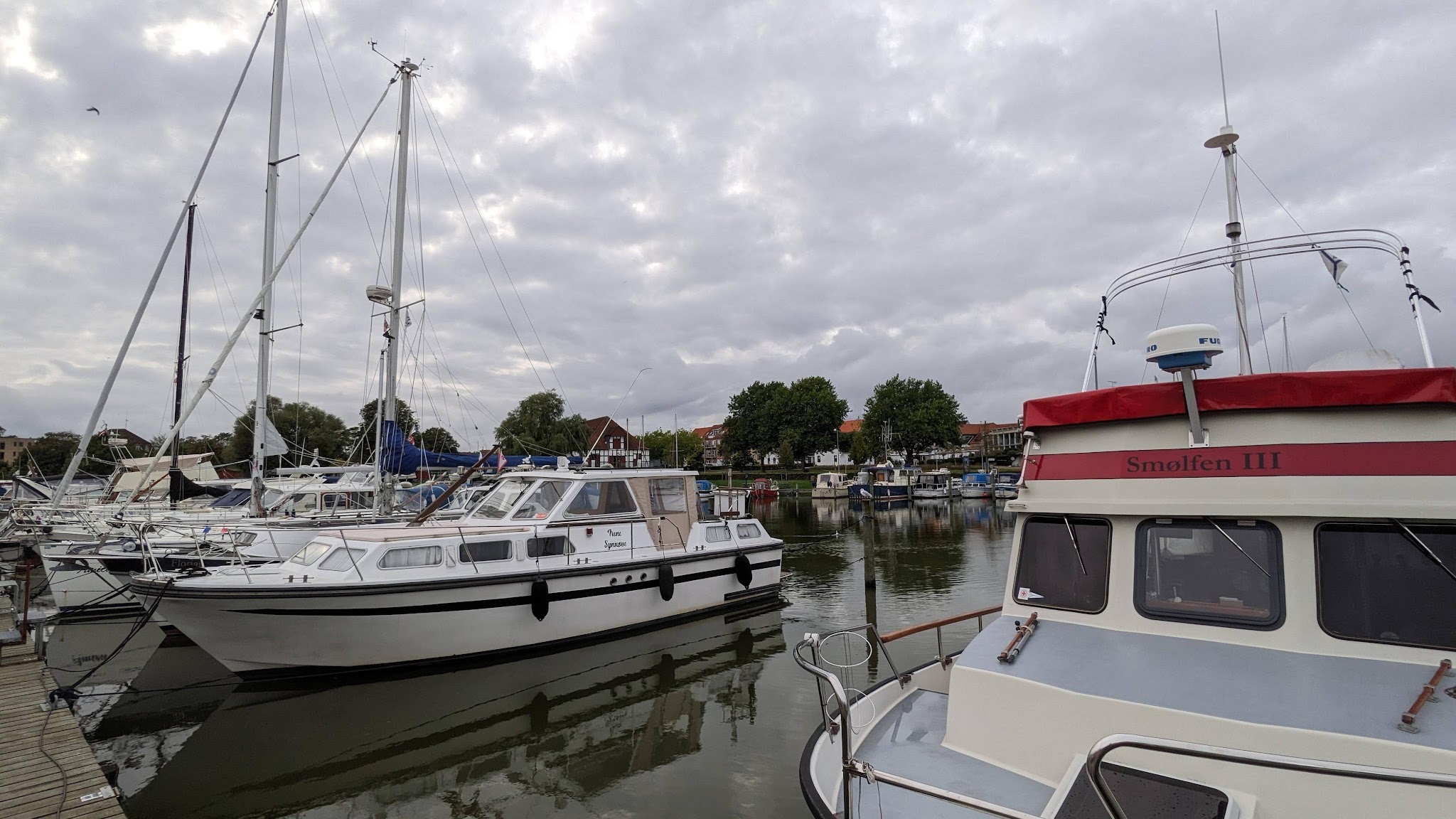 Yachthafen mit mehreren festgemachten Segel- und Motorbooten unter grauem, bewölktem Himmel.