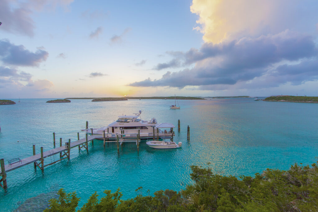 Türkisfarbene Bucht bei Sonnenuntergang, Yacht am Steg, kleines Motorboot daneben, ferne Inseln und Segelboot