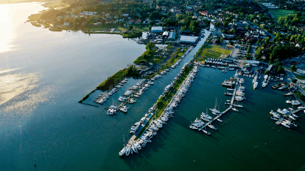 Luftaufnahme eines Yachthafens mit langen Stegen, zahlreichen Segelbooten und angrenzender Kleinstadt am See.