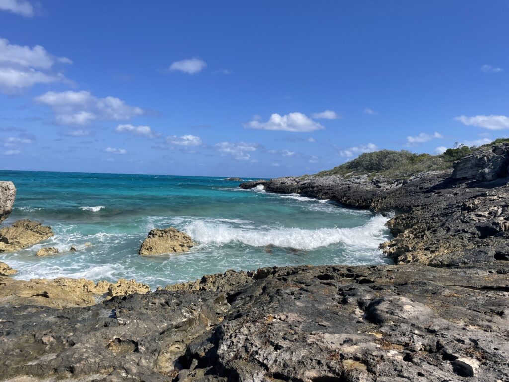 Türkisfarbene Wellen schlagen gegen dunkle, zerklüftete Felsküste unter wolkenlosem, tiefblauem Himmel.