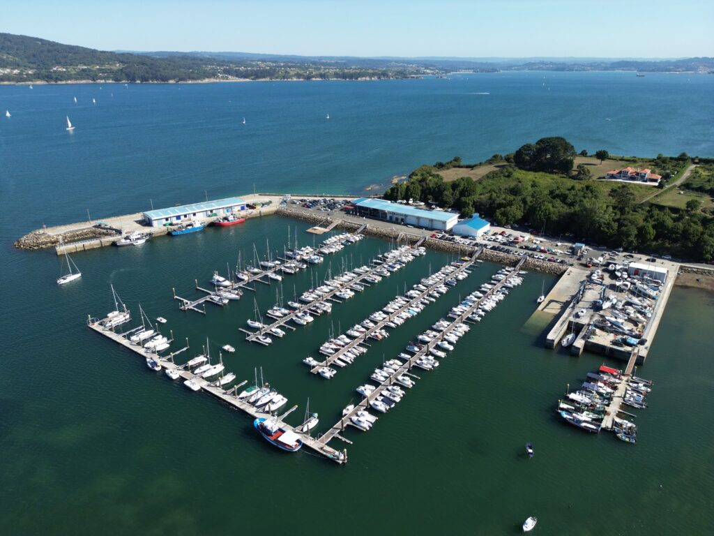 Luftaufnahme eines Yachthafens mit dicht aneinandergereihten Segelbooten, umgeben von blauem Meer und grünen Uferflächen