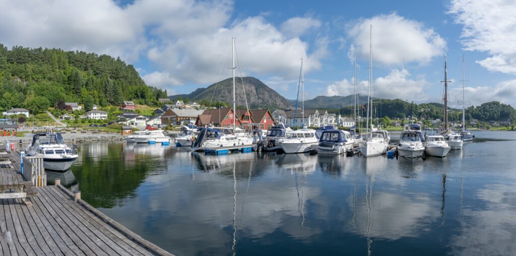 Yachthafen mit weißen Motor- und Segelbooten vor bunten Häusern, grünen Hügeln und Berg unter blauem Himmel