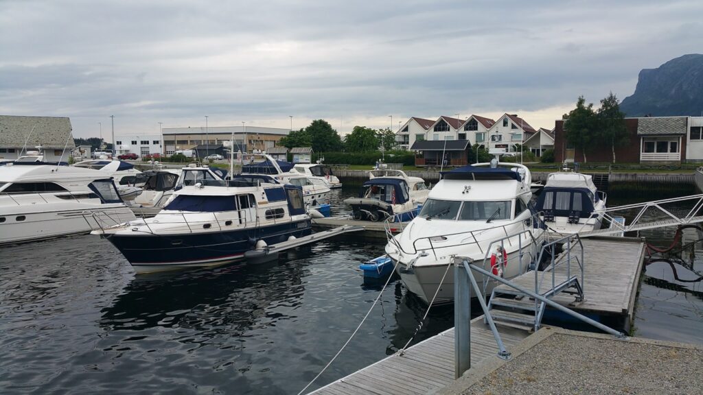 Mehrere Motorboote und Yachten liegen in einem kleinen Hafen vor Wohnhäusern unter bewölktem Himmel.