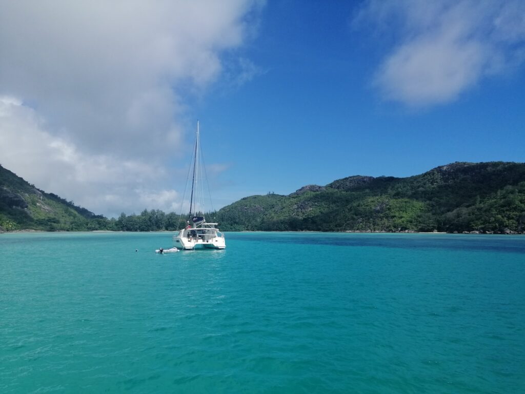 Katamaran ankert im klaren türkisfarbenen Wasser vor grünen Hügeln unter blauem Himmel mit Wolken