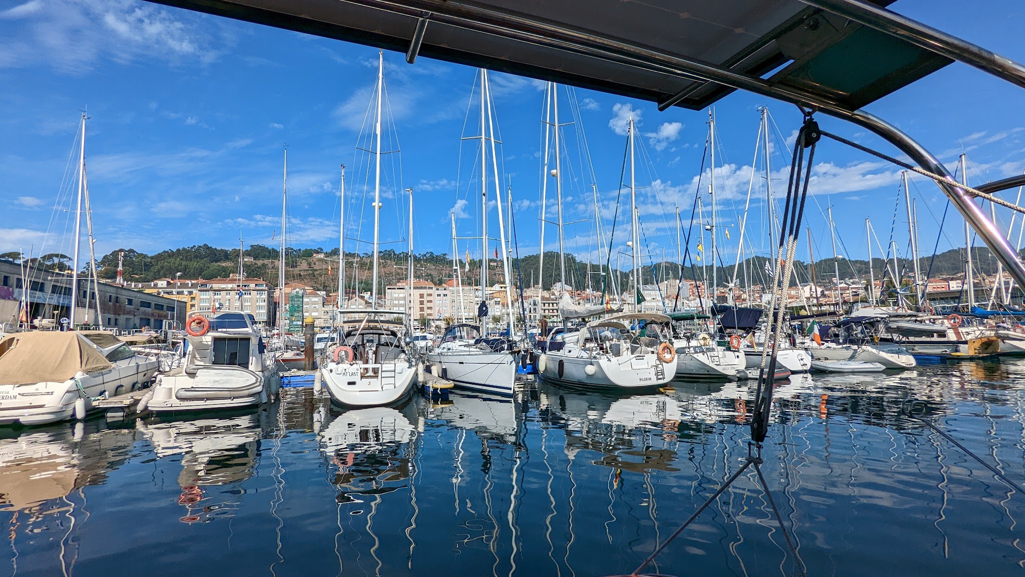 Segelboote liegen dicht an dicht im Yachthafen; Masten spiegeln sich im ruhigen, blau glitzernden Wasser.