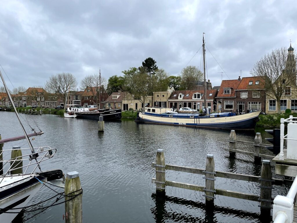 Kleiner Hafenkanal mit historischen Segelbooten vor Backsteinhäusern mit roten Giebeln unter bewölktem Himmel.