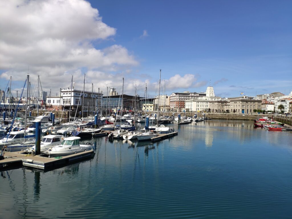 Sonniger Hafen mit zahlreichen Segel- und Motorbooten; ruhiges Wasser spiegelt blauen Himmel und Stadthäuser.