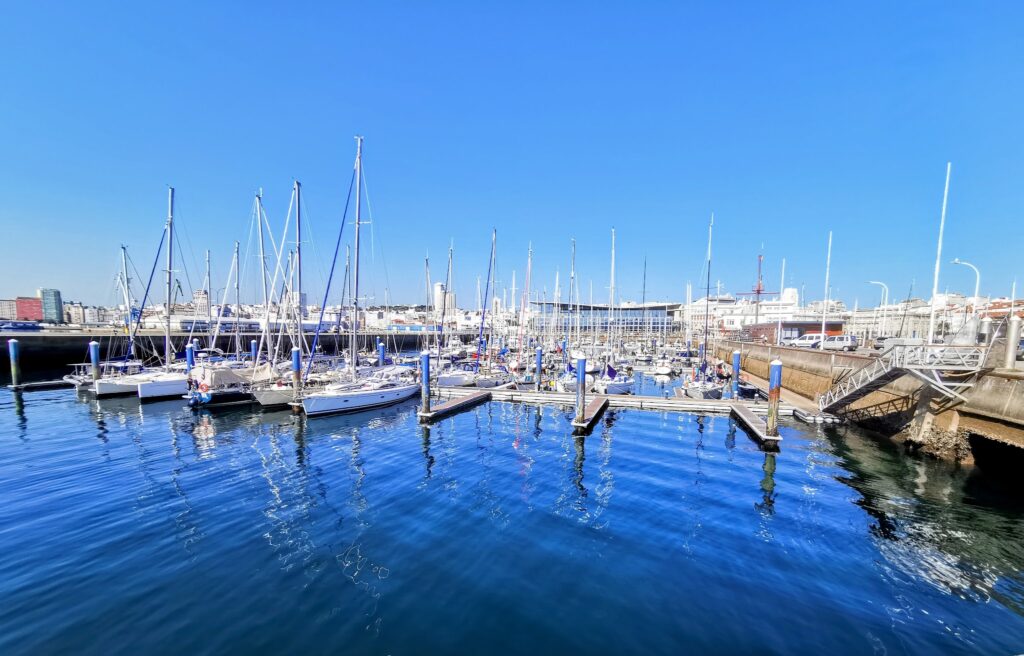 Yachthafen mit zahlreichen Segelbooten am klarblauen Wasser unter wolkenlosem Himmel, Stadt im Hintergrund.