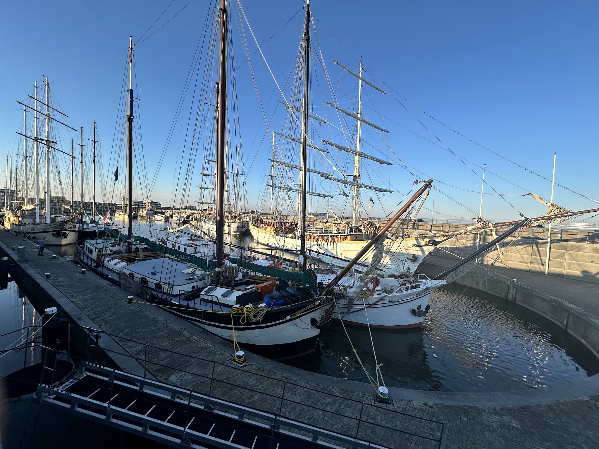 Mehrere historische Segelschiffe mit hohen Masten liegen an einem sonnigen Hafenpier unter klarem Himmel.