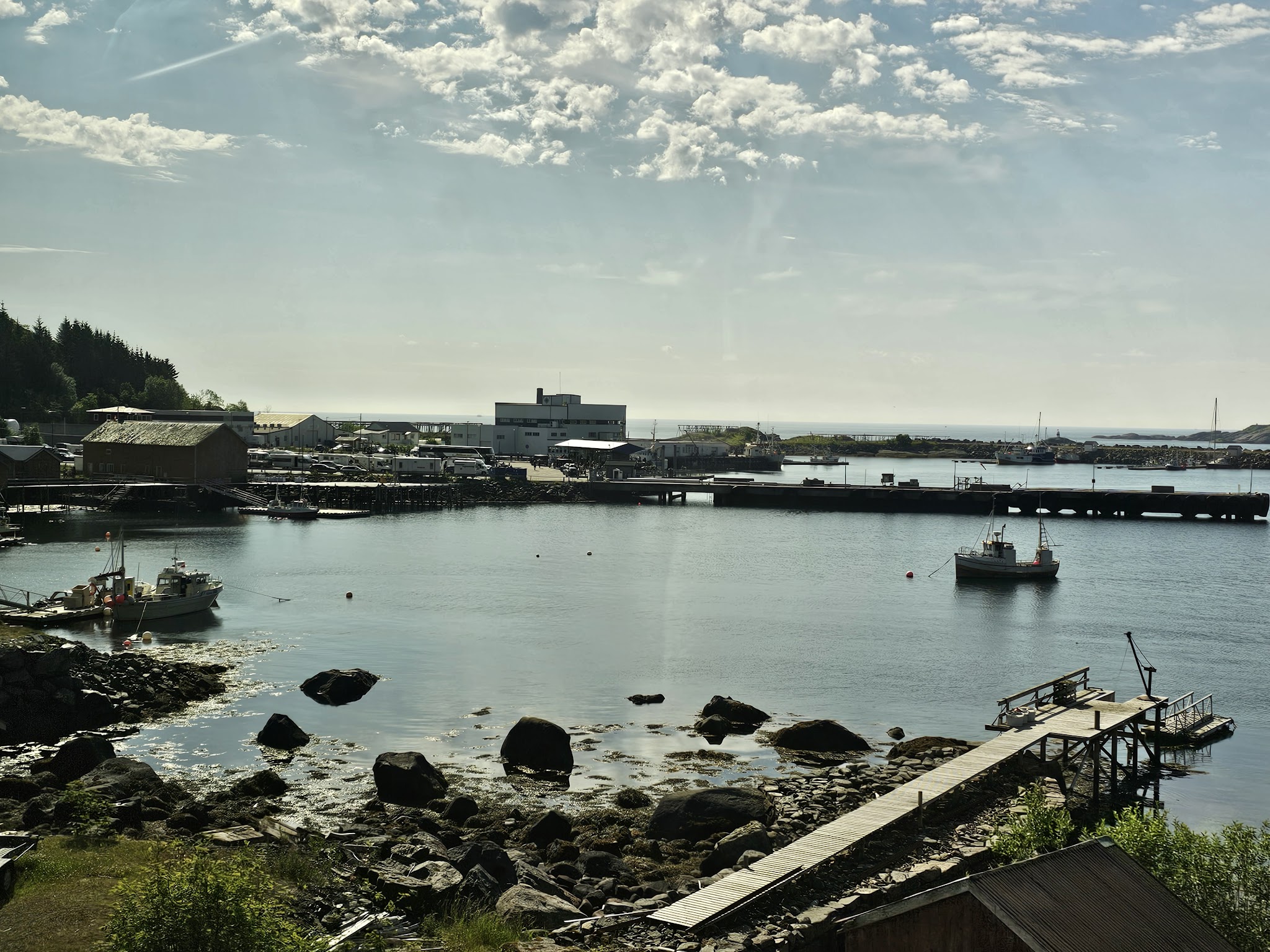Kleiner Hafen mit zwei Fischerbooten, Holzsteg und felsiger Küste unter leicht bewölktem Himmel.