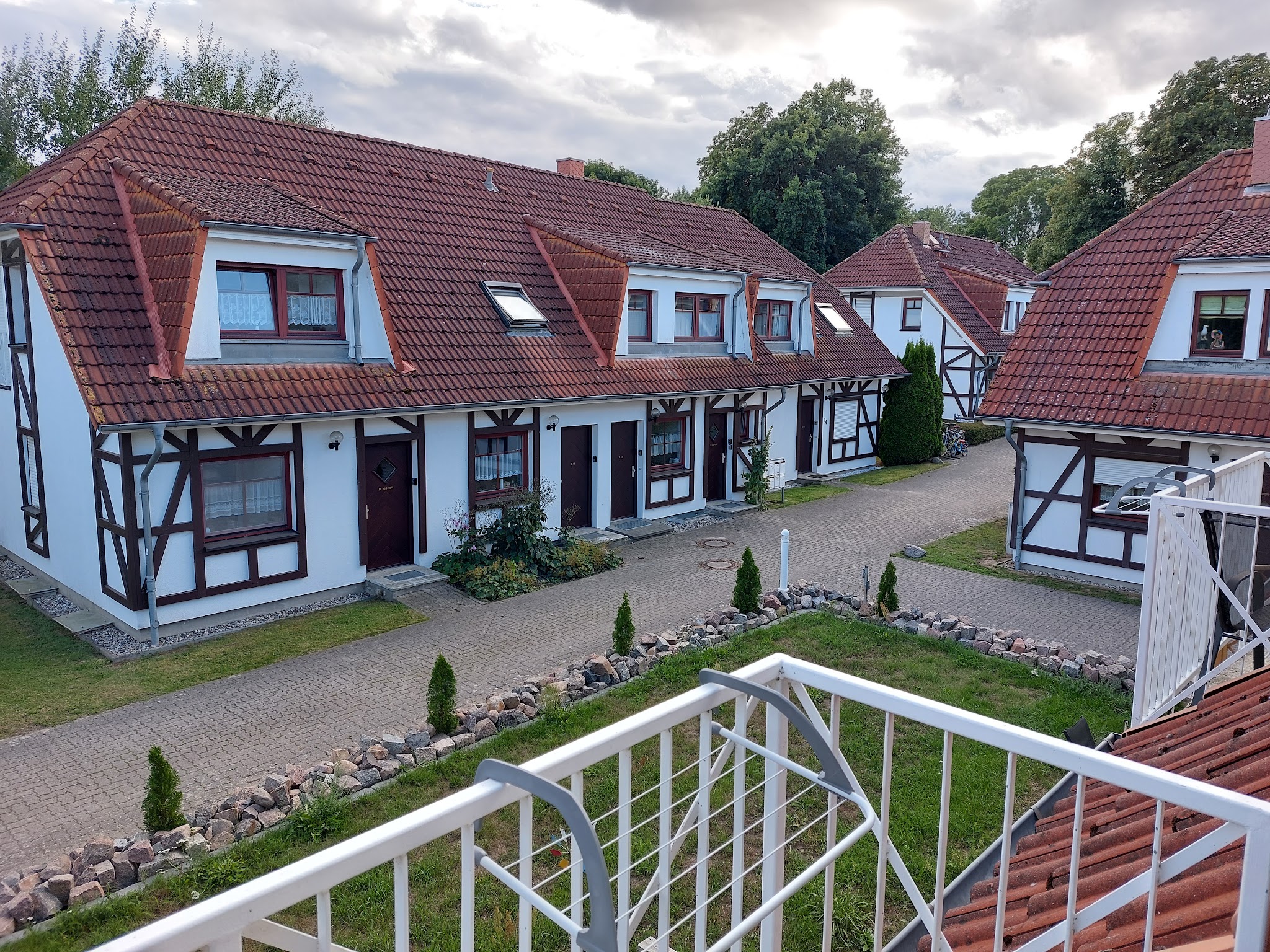 Blick von Balkon auf Reihenfachwerkhäuser mit roten Ziegeldächern, gepflastertem Weg und kleinem begrüntem Hof.
