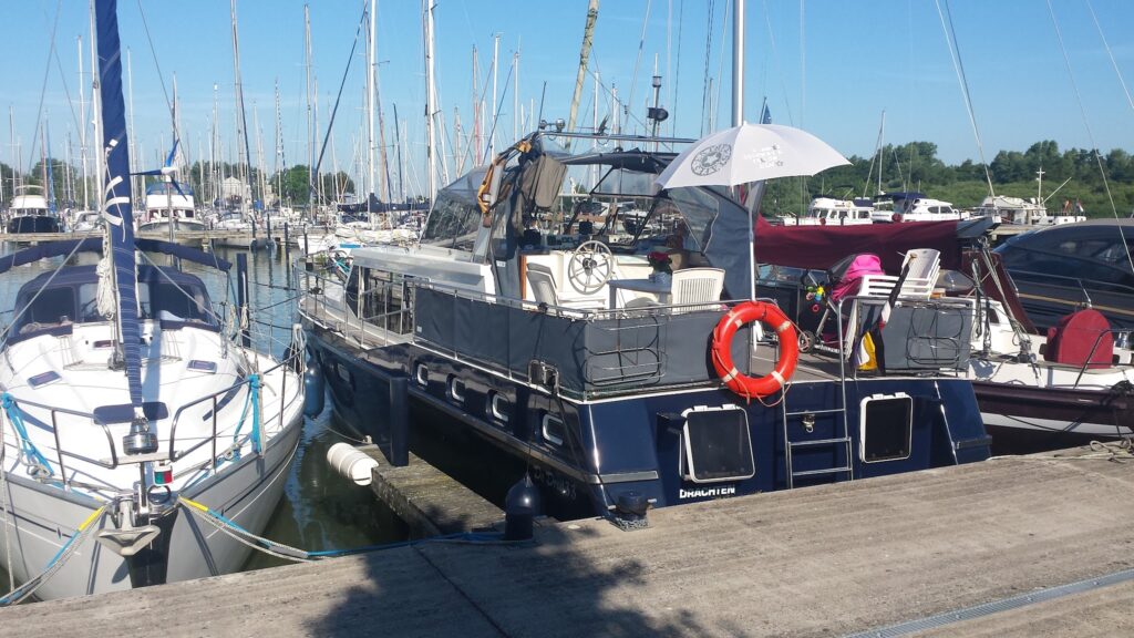 Sonniger Hafen: Dunkelblaues Motorboot mit Rettungsring und weißem Sonnenschirm liegt zwischen Segelyachten.