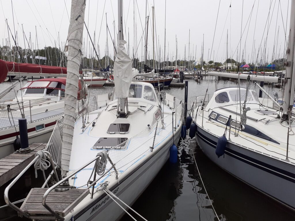 Segelyachten dicht nebeneinander im Hafen, schmale Stege, viele Masten ragen bei grauem Himmel in die Höhe.