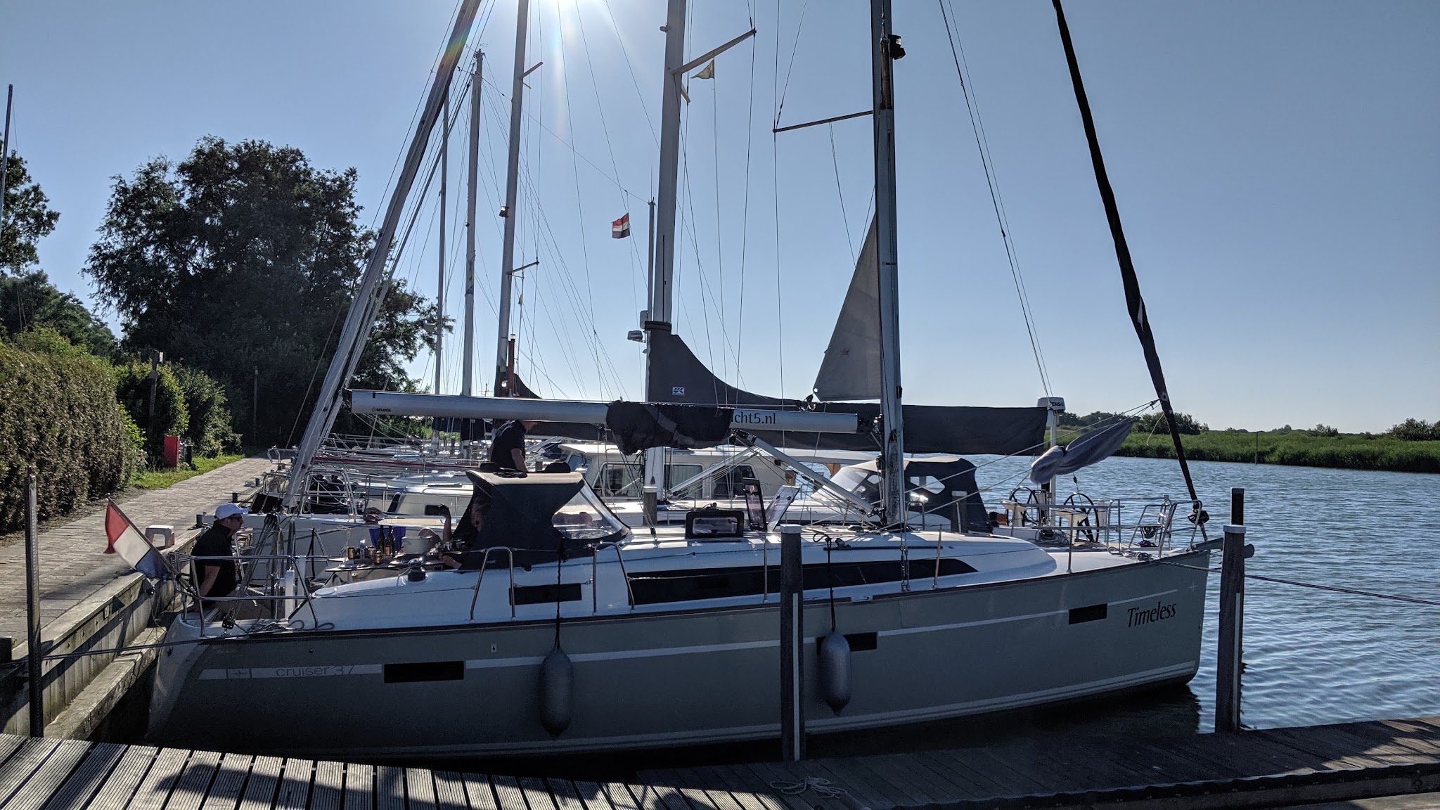 Segelyacht „Timeless“ liegt bei Sonnenschein am Steg; eingeholtes Segel, niederländische Flagge, ruhiges Wasser.