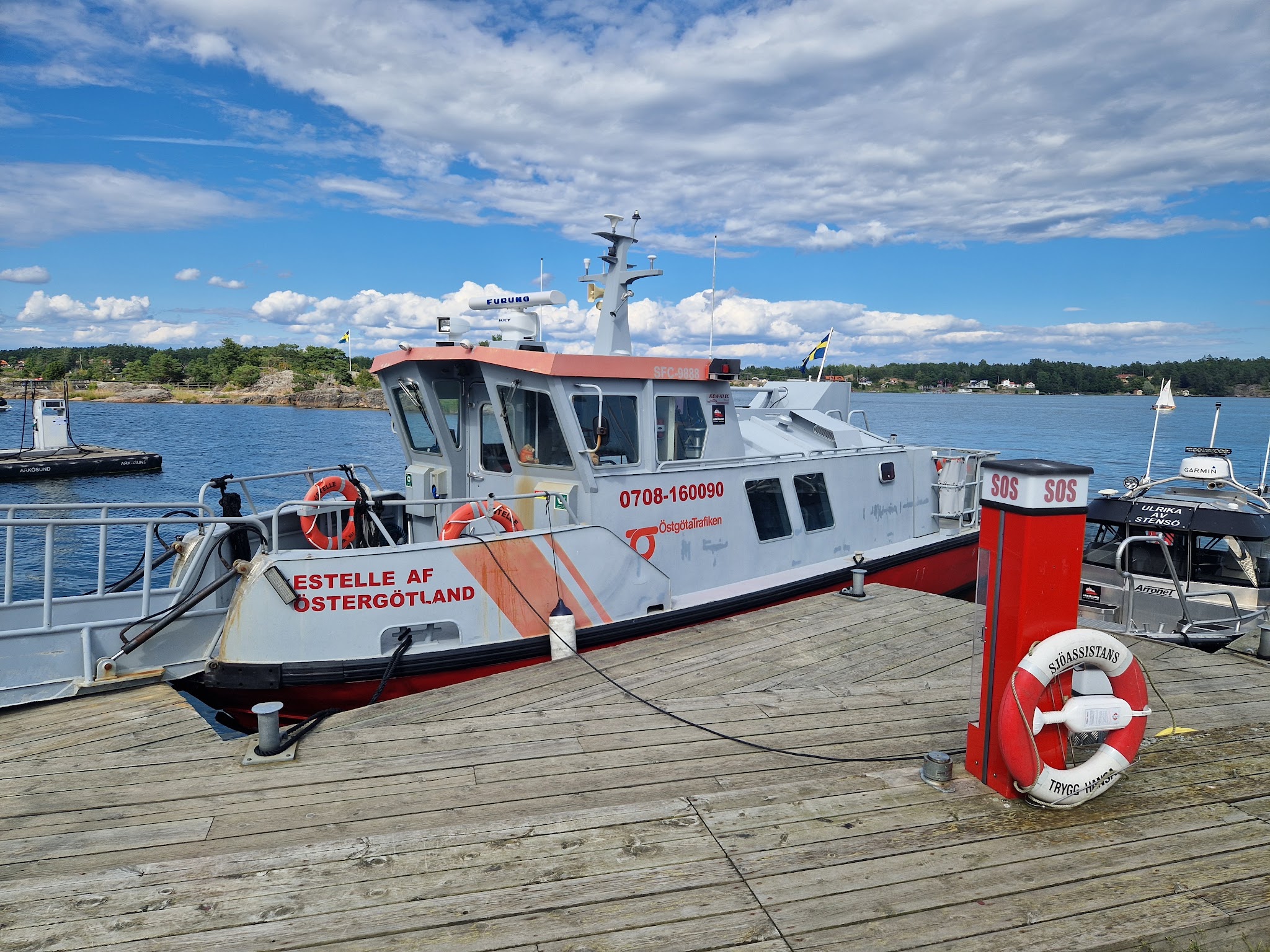 Rettungsboot „Estelle af Östergötland“ liegt am Holzsteg; SOS-Rettungsring und schwedische Schären im Hintergrund.
