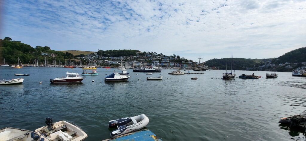 Ruhiger Hafen mit vielen kleinen Booten; bunt bebaute, bewaldete Hangkulisse unter leicht bewölktem Himmel.