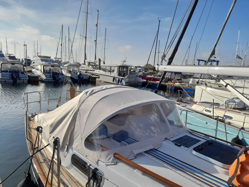 Segelboot mit hellen Persenning im Vordergrund, umgeben von zahlreichen Booten im sonnigen Yachthafen.