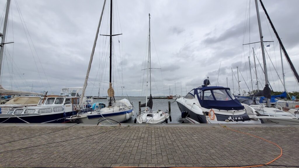 Segel- und Motorboote liegen nebeneinander im ruhigen Hafen, darüber dichter grauer Himmel.
