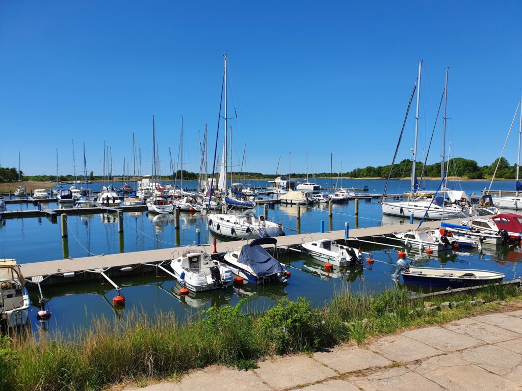 Yachthafen mit zahlreichen Segel- und Motorbooten an Stegen; ruhiges Wasser unter wolkenlosem Himmel