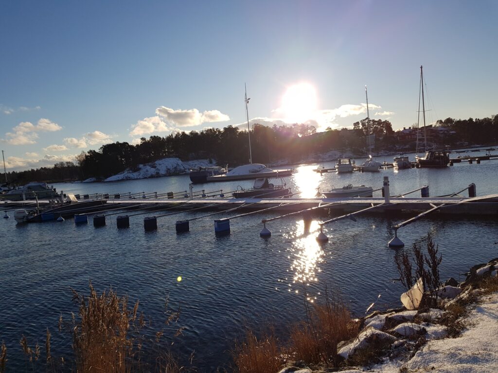 Tiefer Wintersonne spiegelt sich im ruhigen Hafen; vereinzelt vertäute Segelboote, schneebedeckte Ufer
