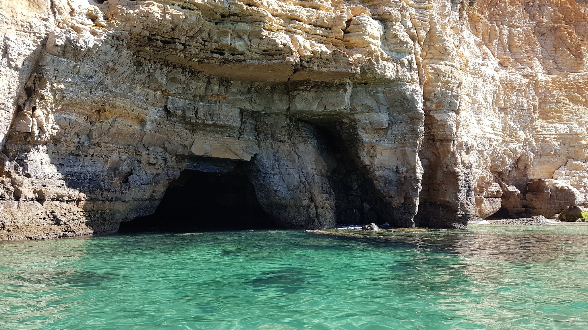 Türkisgrünes Meerwasser vor hellen Kalkfelsen mit dunkler Meeresgrotte.
