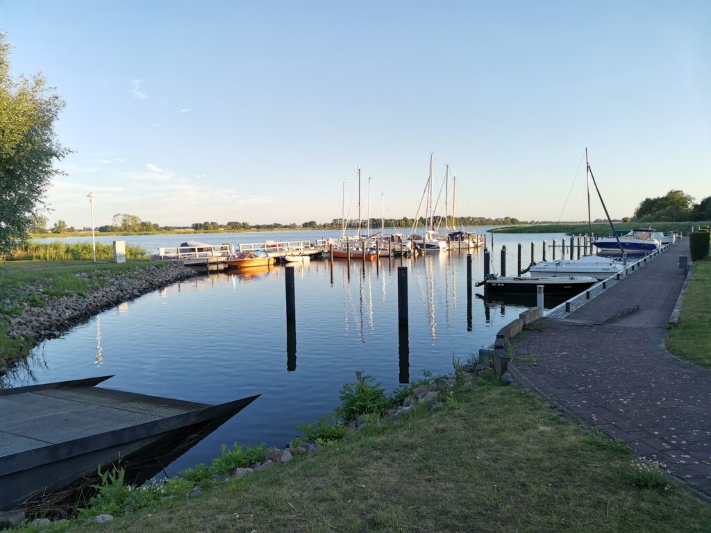 Kleiner Hafen bei ruhigem Wasser, mehrere Segel- und Motorboote am Steg, Abendlicht, klarer Himmel
