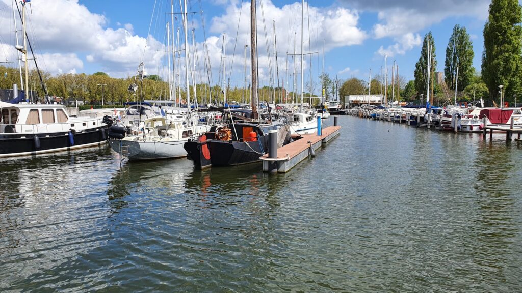 Yachthafen mit anliegenden Segel- und Motorbooten an Schwimmstegen, ruhiges Wasser, blauer Himmel mit Wolken