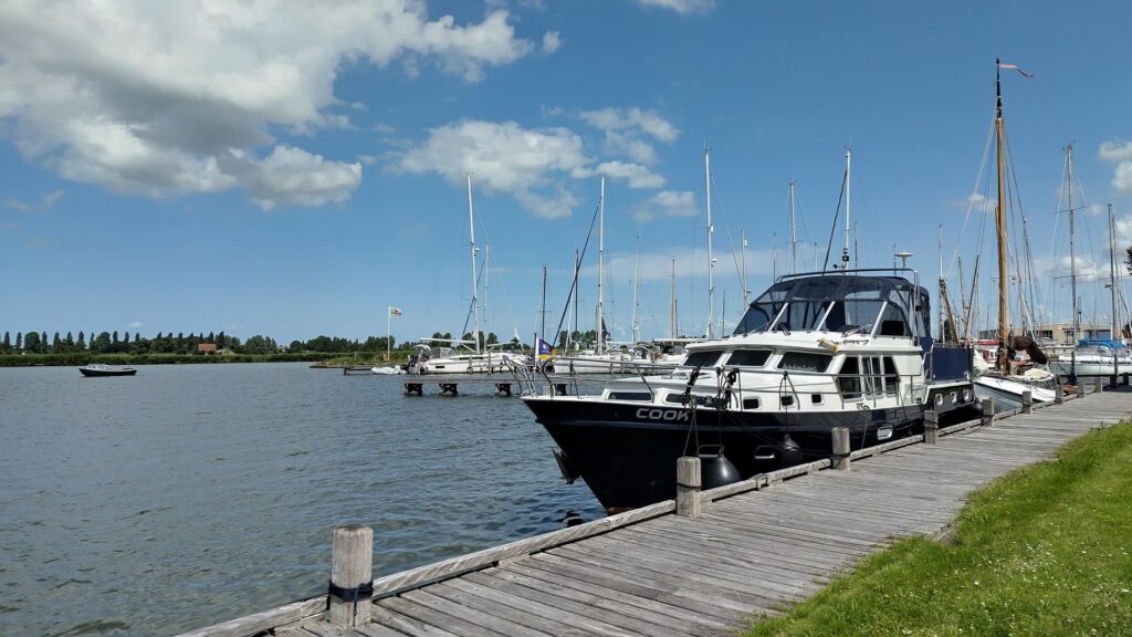 Yachten liegen an hölzernem Steg im Hafen; ruhiges Wasser und blauer Himmel mit wenigen Wolken