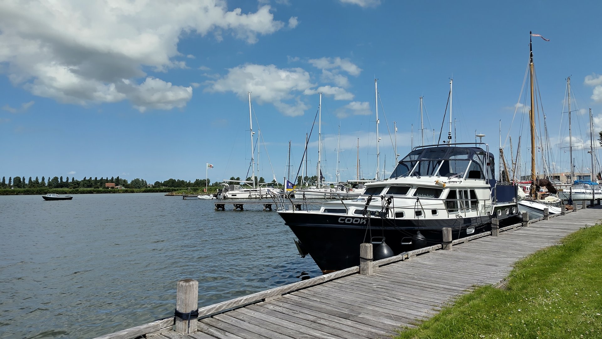 Yachten liegen an hölzernem Steg im Hafen; ruhiges Wasser und blauer Himmel mit wenigen Wolken