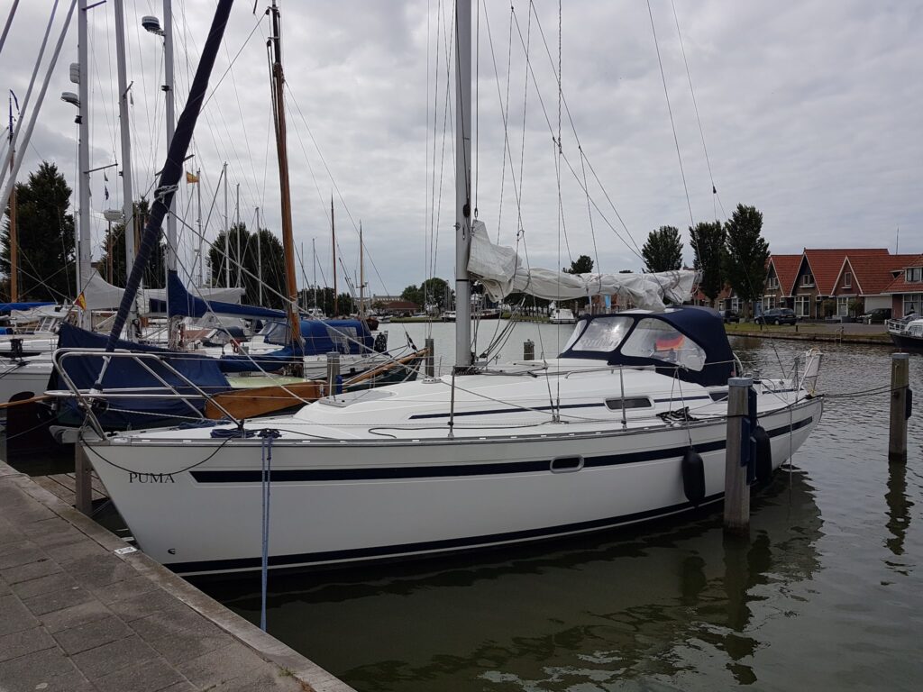 Weißes Segelboot namens „Puma“ liegt im Yachthafen, umgeben von weiteren Booten und roten Giebelhäusern.