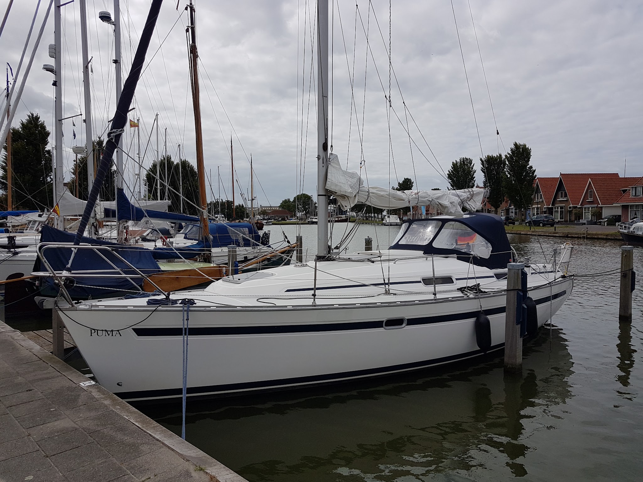 Weißes Segelboot namens „Puma“ liegt im Yachthafen, umgeben von weiteren Booten und roten Giebelhäusern.