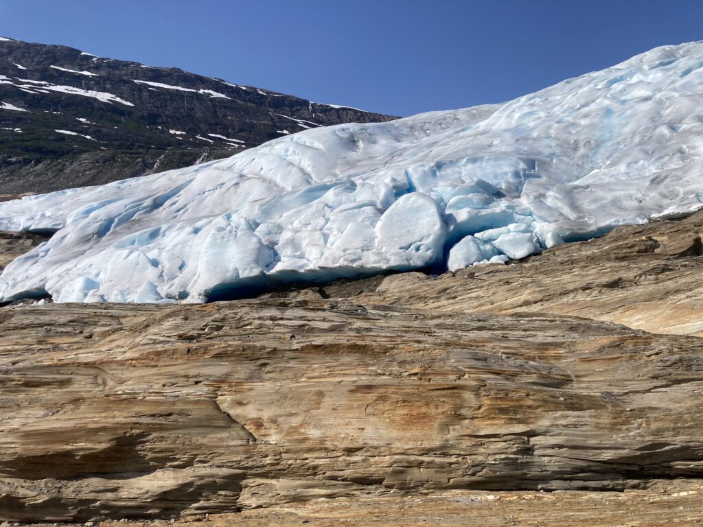 Hellblauer Gletscher breitet sich über braune Felsplatten aus, kontrastiert vor wolkenlosem Himmel.